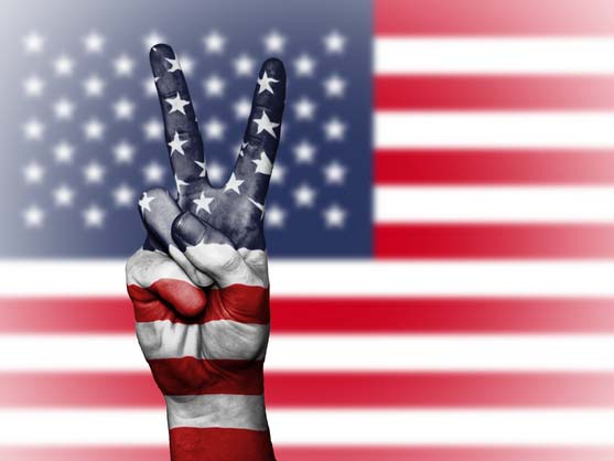 A hand showing the peace sign in front of the USA flag